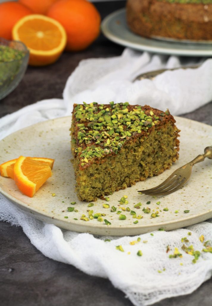 Wedge of pistachio cake on plate with orange slices and fork.