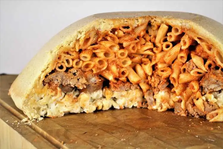 Pasta and meatballs layered in savory pastry dome on wood board.