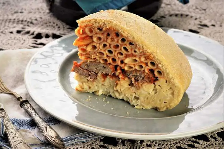 Wedge of timpano pasta bake in crust on plate.