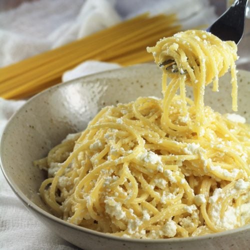 Creamy sauce pasta in bowl with forkful.