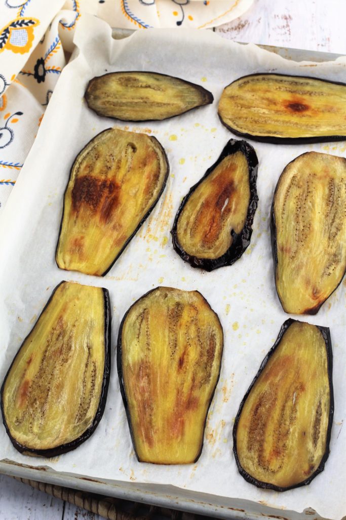 Roasted eggplant slices on parchment covered baking sheet.