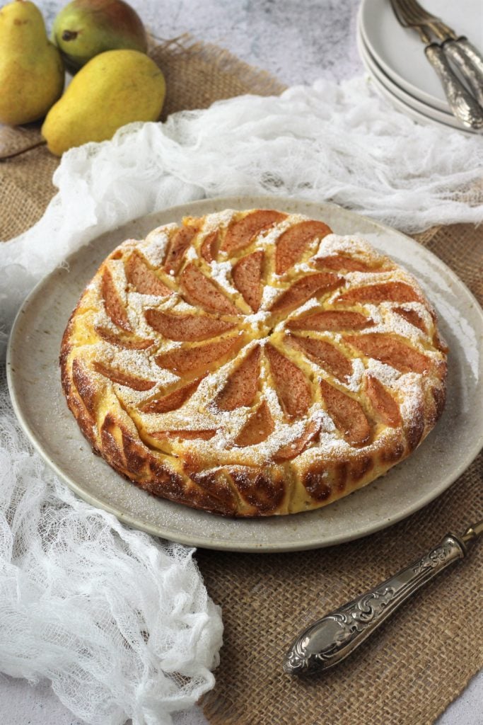 Ricotta cheesecake topped with pear slices on plate.