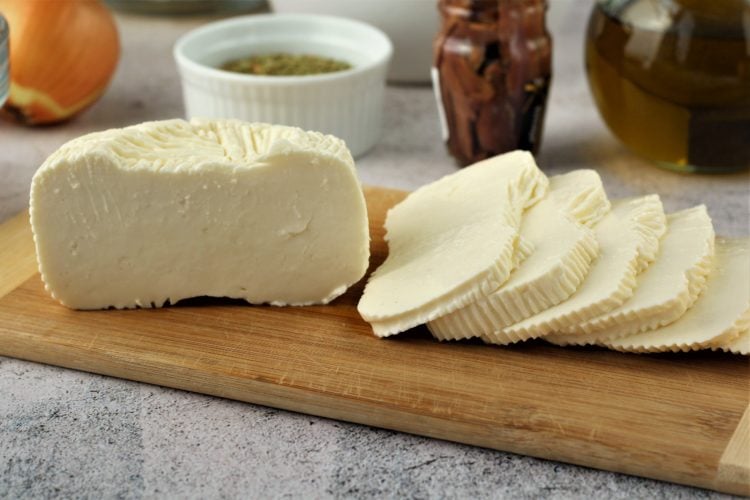 Sliced white tuma cheese on wood board.
