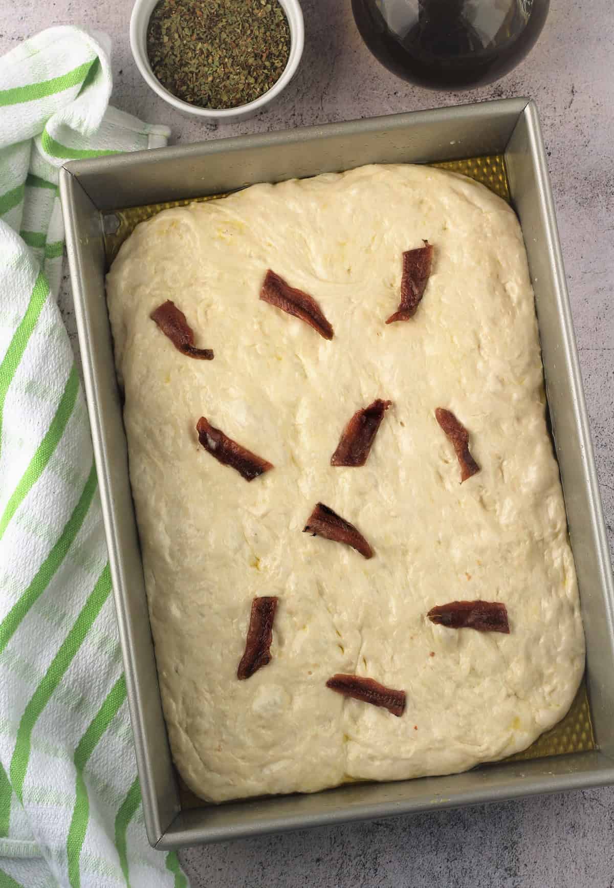 Sfincione dough topped with anchovies in rectangular pizza pan.