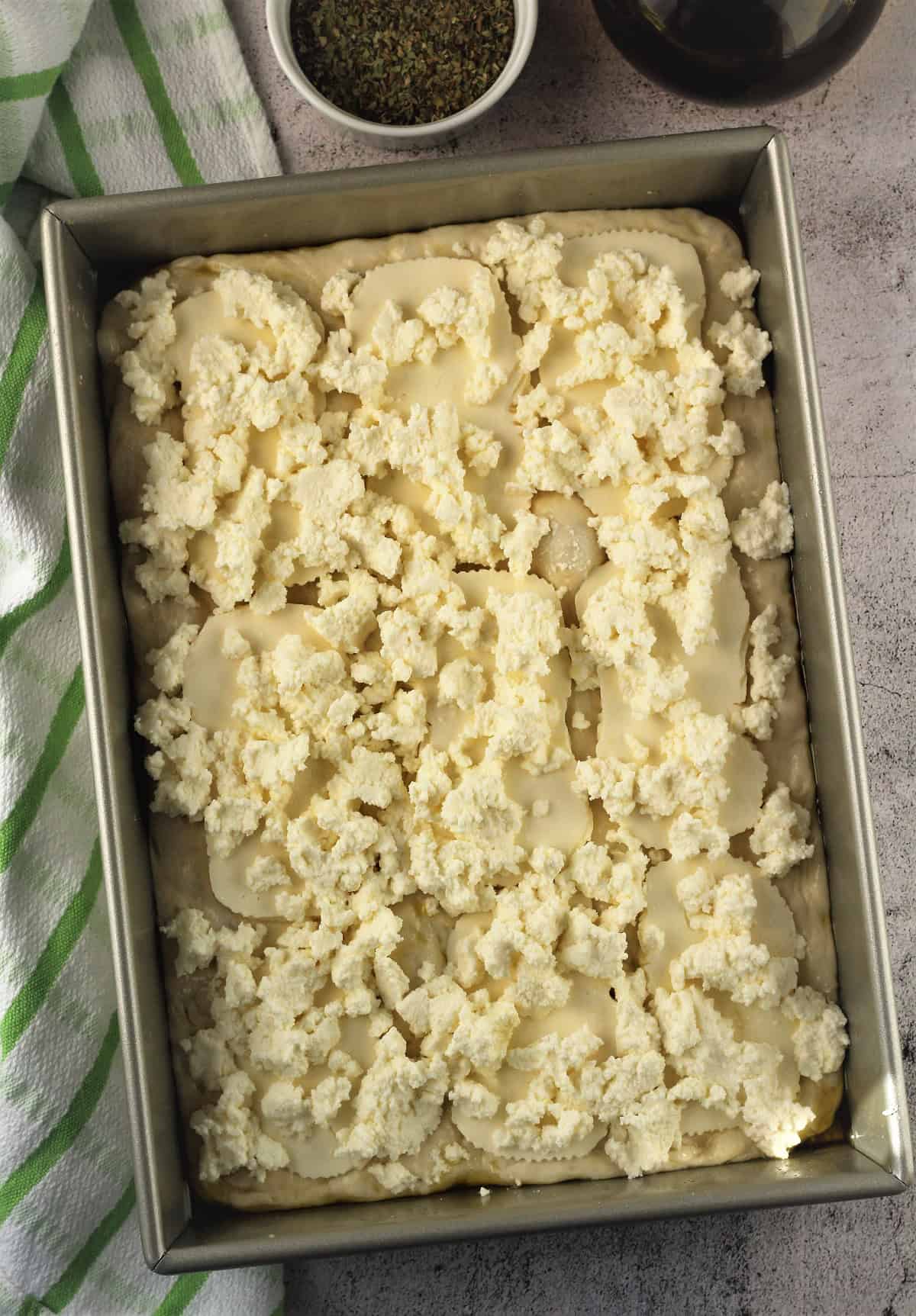 Dollops of ricotta on top of sfincione dough in rectangular pizza pan.