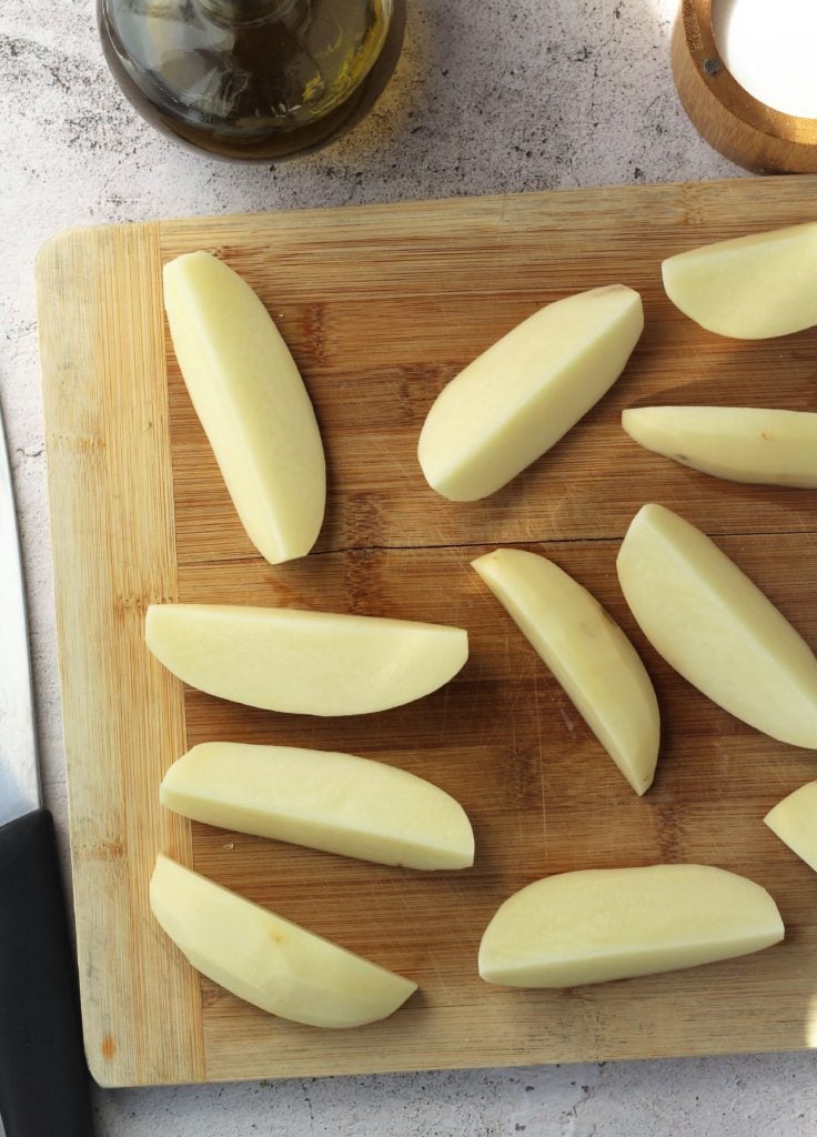 Quartered potato wedges on wood board.