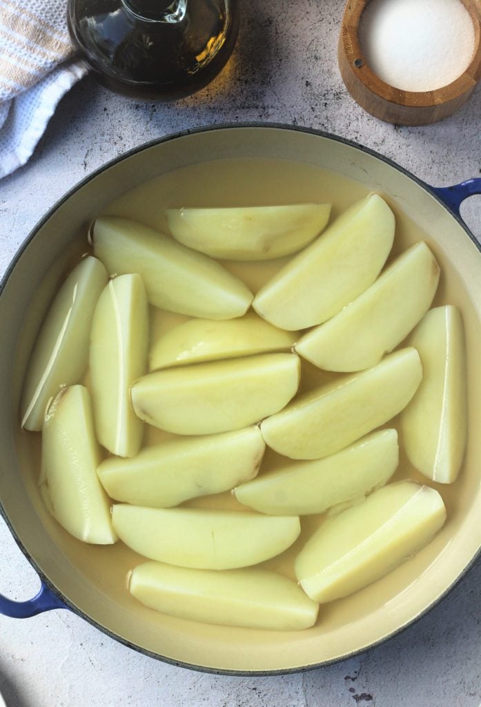 Potato wedges boiling in skillet.