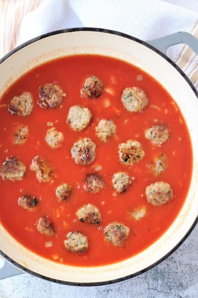 Meatballs nestled in tomato sauce in skillet.