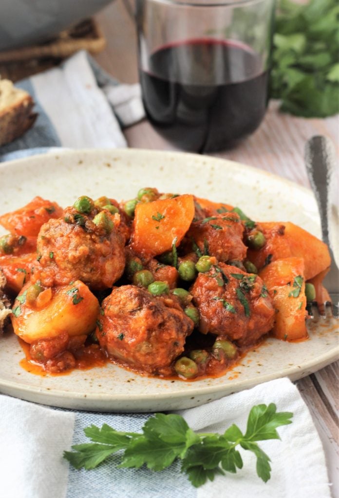 Plate with meatballs, potatoes and peas in tomato sauce.