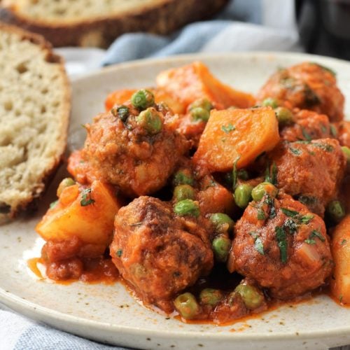 Meatball stew with potatoes and peas on plate.