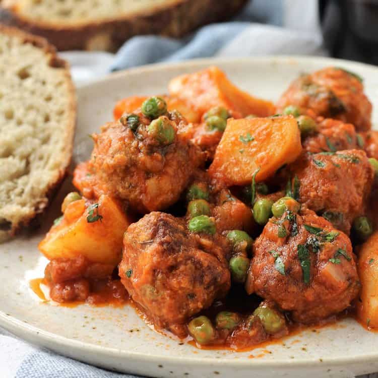 Meatball stew with potatoes and peas on plate.
