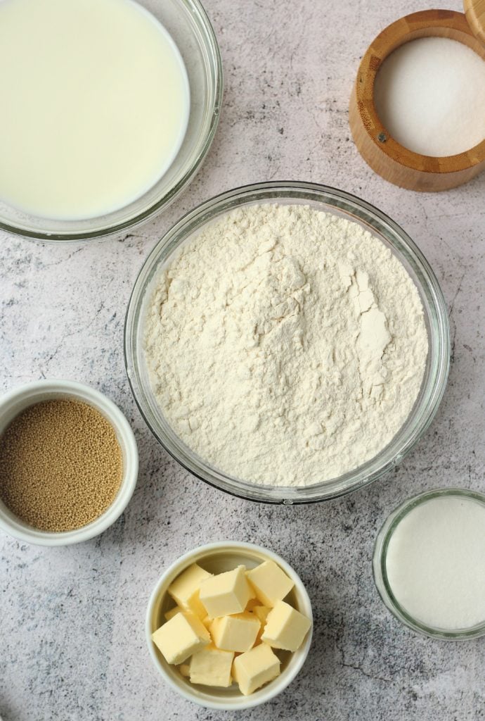 Flour, sugar, butter, yeast, salt and milk in bowls.