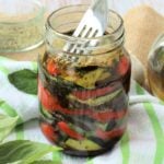 Fork pressing down on marinated roasted vegetables layered in jar.