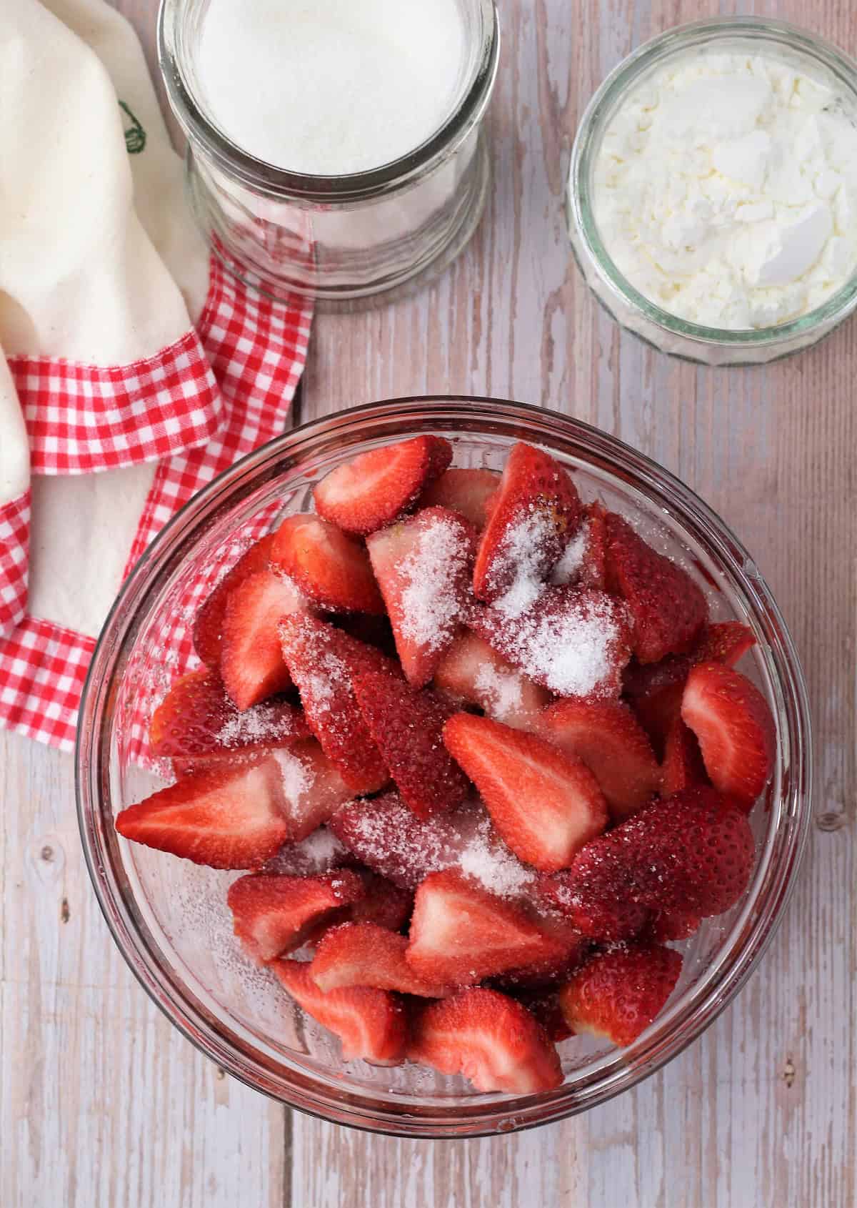 Chopped strawberries in glass bowl tossed with granulated sugar for gelo di fragole recipe.