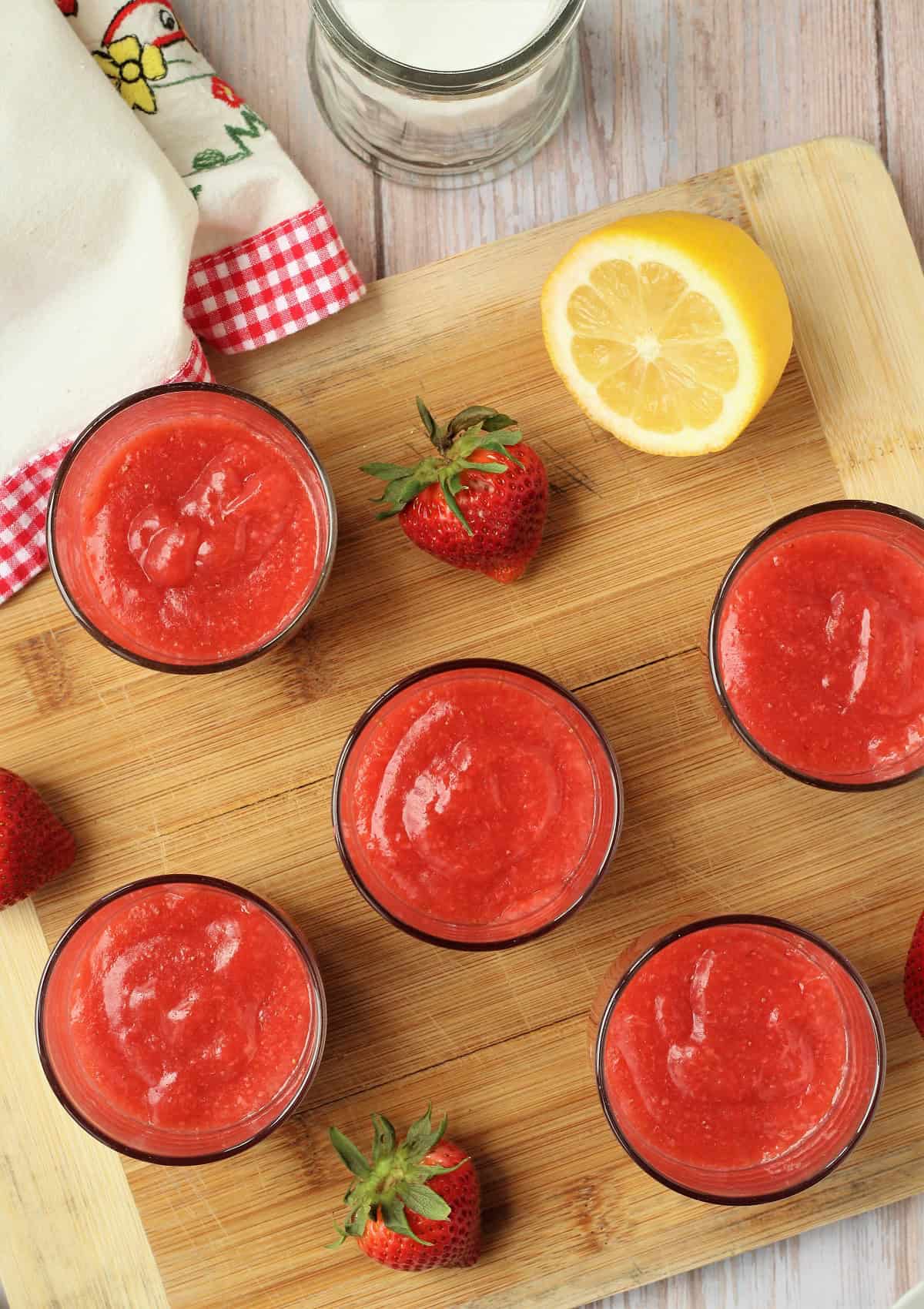 Sicilian strawberry pudding poured into glasses surrounded by strawberries and lemon half.