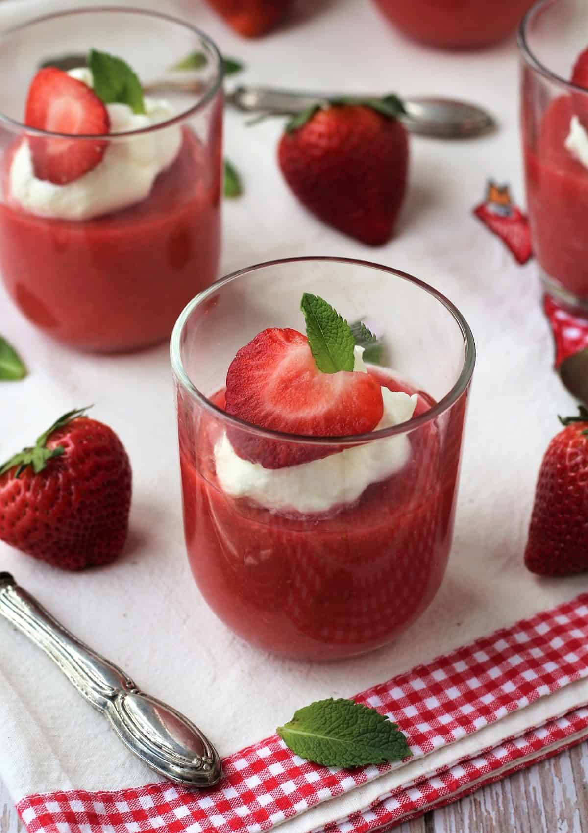 Gelo di fragole in glasses topped with whipped cream, strawberry half and mint leaf.