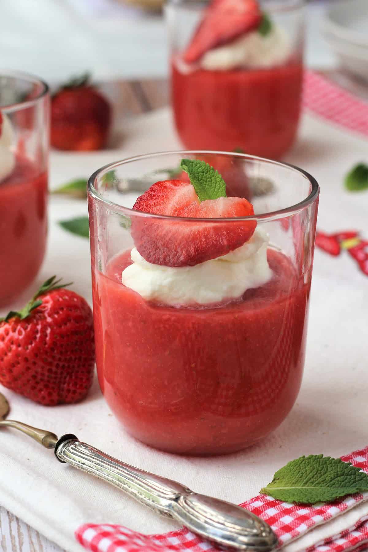 Sicilian strawberry pudding (gelo di fragole) in glasses topped with whipped cream strawberry half and mint leaf.