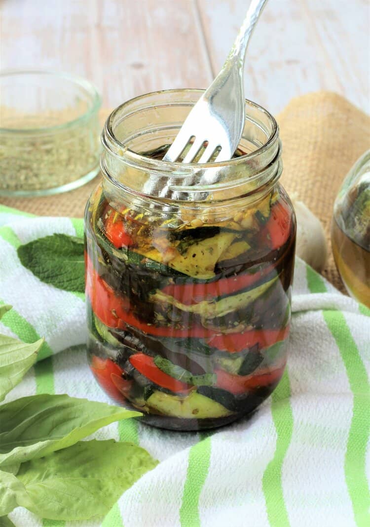 Fork pressing down on layered roasted vegetables in jar.