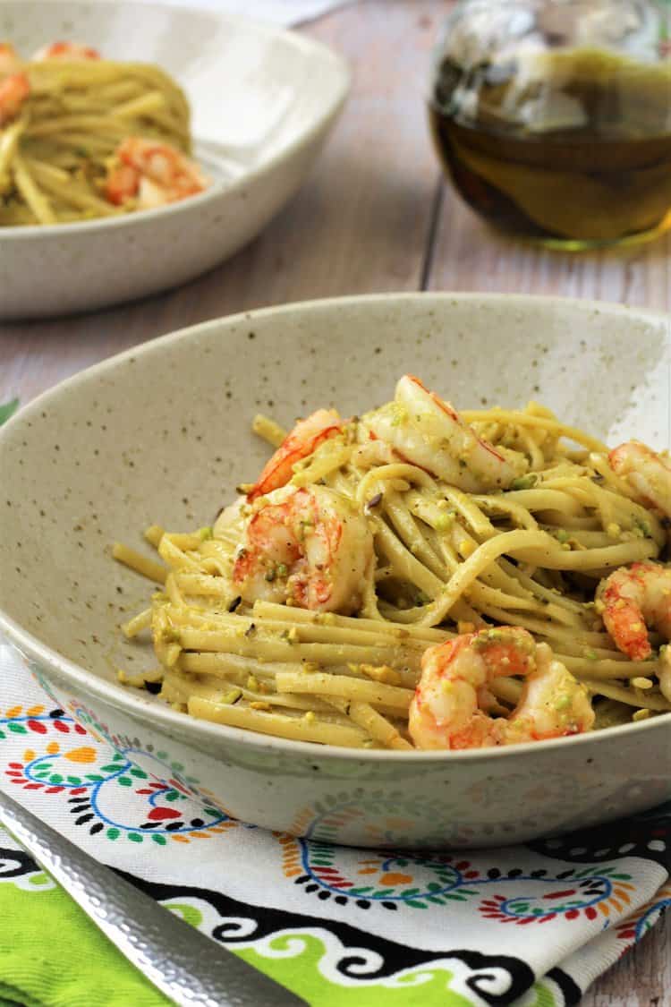 Plated pesto shrimp pasta with olive oil bottle.