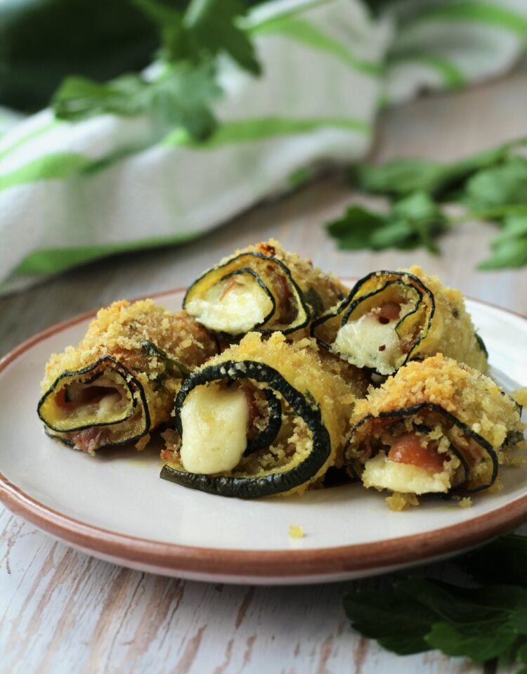 Zucchini roll ups with prosciutto and cheese piled on plate.