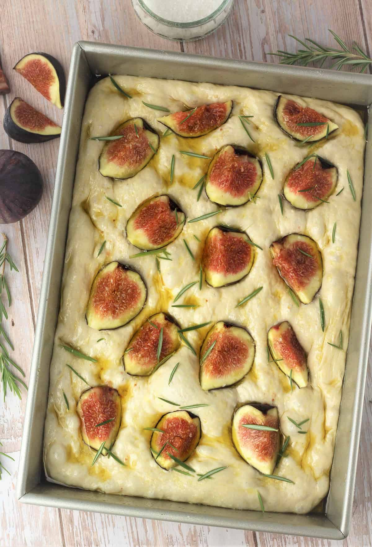 Focaccia dough in rectangular pan topped with figs and rosemary.