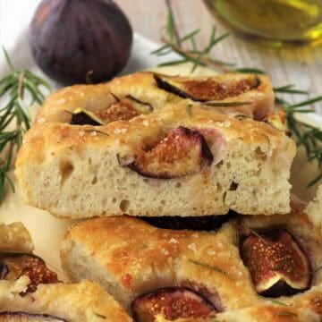 No knead fig and rosemary focaccia squares piled next to fig, olive oil bottle and rosemary figs.