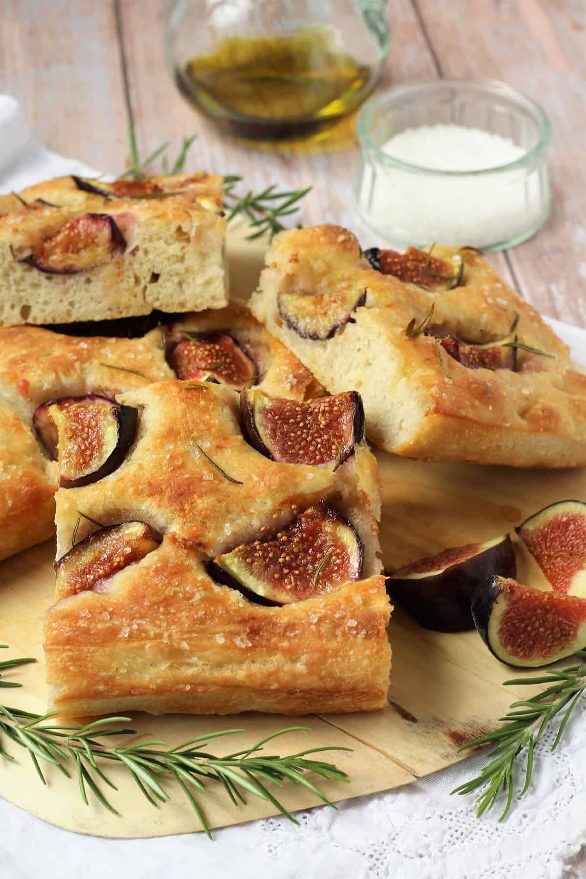 No knead fig and rosemary focaccia squares piled on wood board with rosemary sprigs.