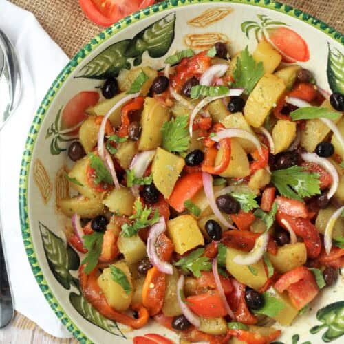 Italian potato salad with roasted red peppers and tomatoes in large bowl.