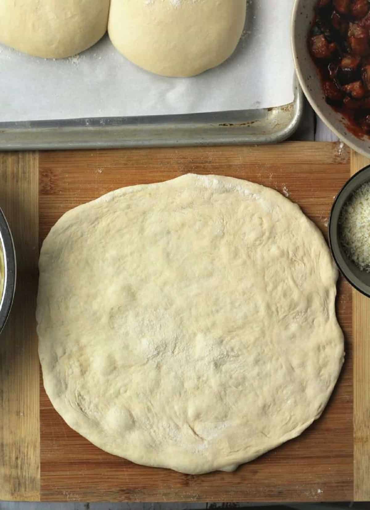 Flattened no knead pizza dough into circular shape on wood board.