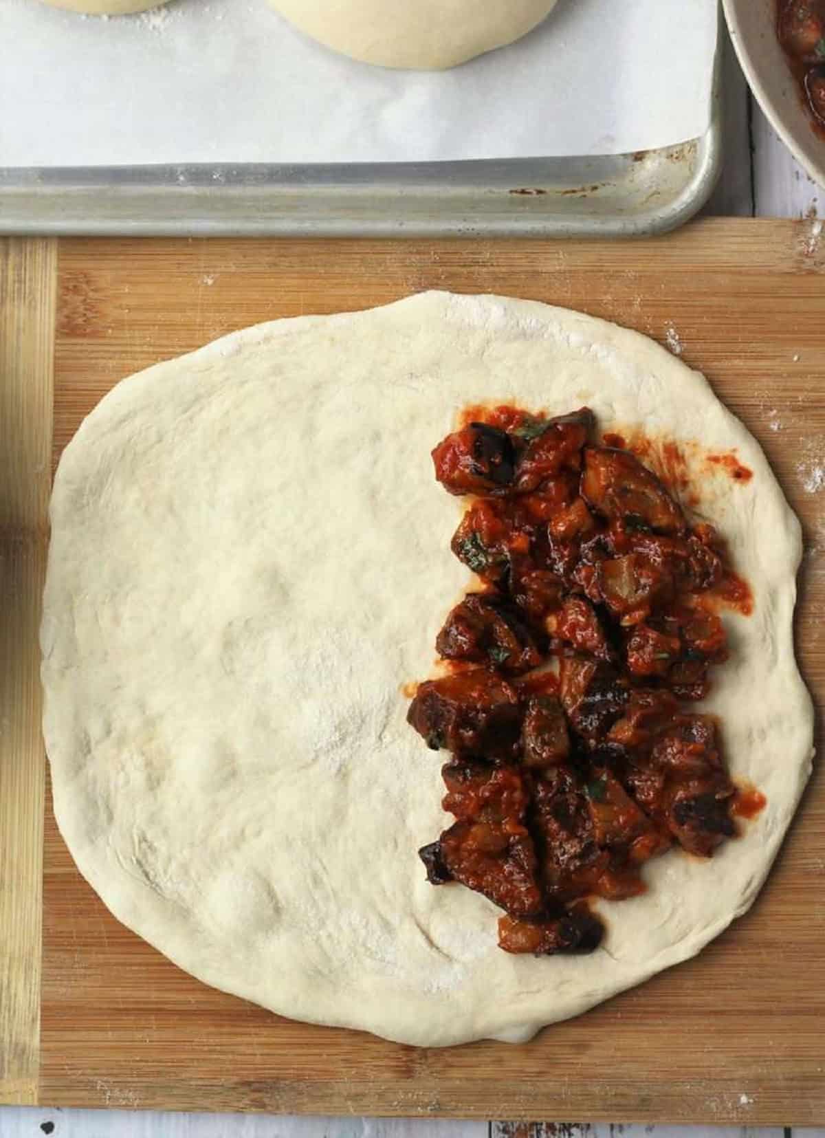 Eggplant filling on one half offlattened round pizza dough.