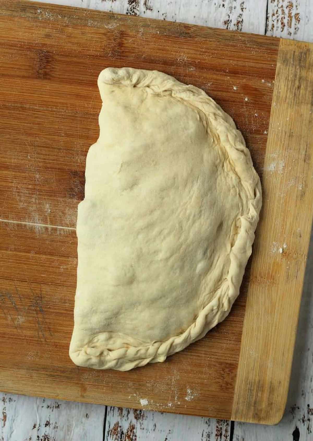 Eggplant filled calzone shaped into half moon on wood board.