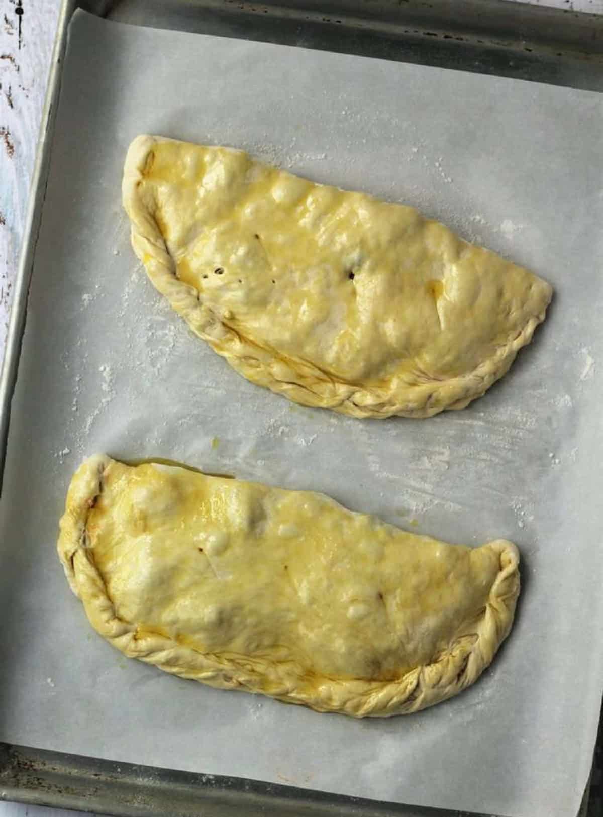 Unbaked calzone brushed with olive oil on baking sheet.