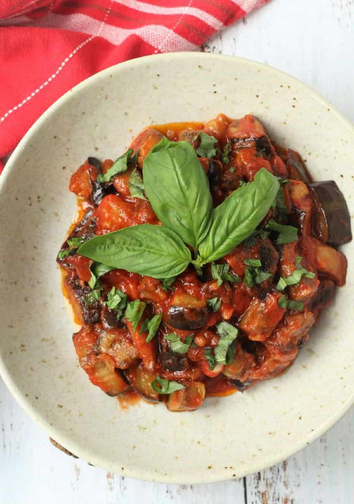 Plated eggplant alla Norma sauce topped with fresh basil.