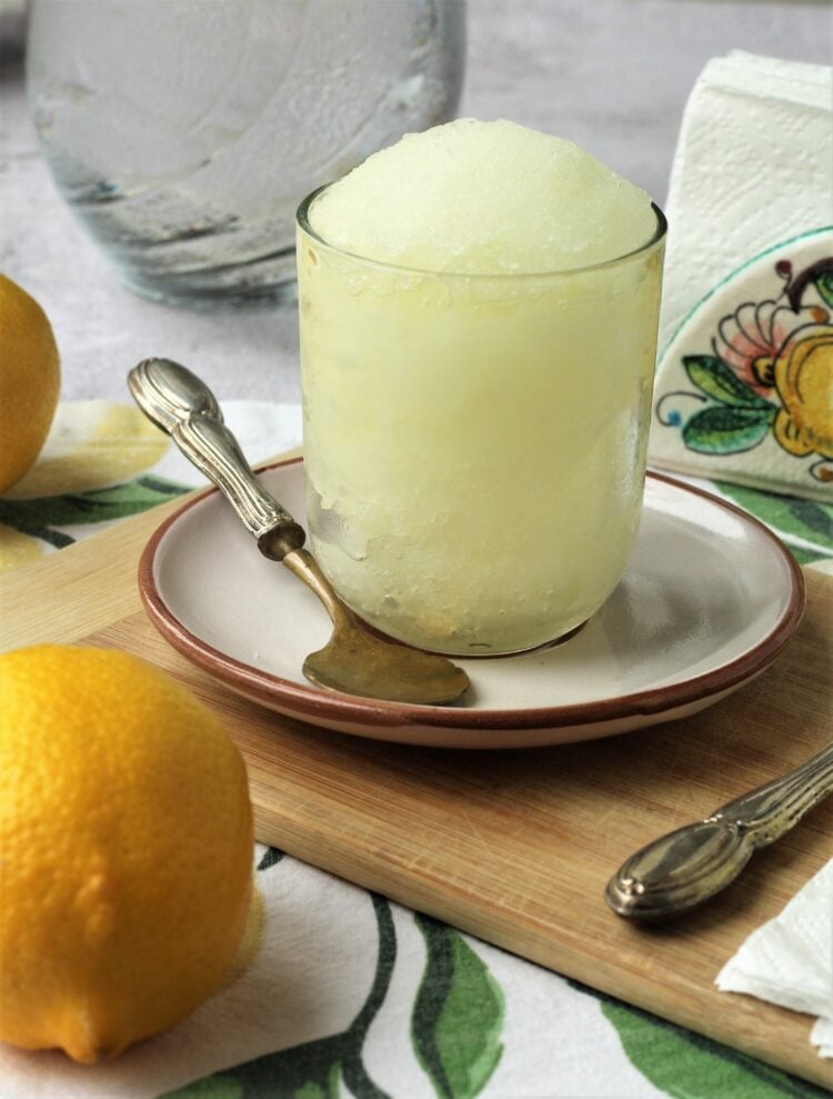 Glass filled with granita al limone on plate with spoon.