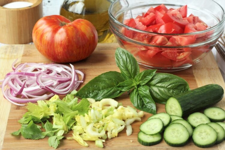 Sliced tomatoes, cucumber, celery and onions on wood board.