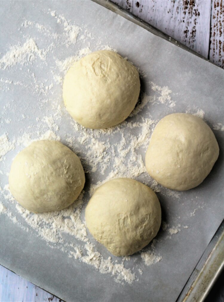 Four pizza dough balls on baking sheet.