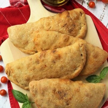 Eggplant calzone alla Norma on wood board with cherry tomatoes and olive oil bottle on the side.
