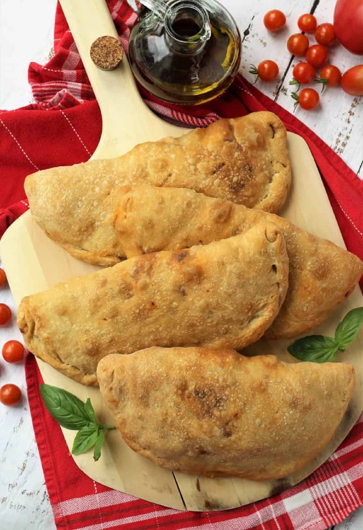 Eggplant calzone alla Norma on wood board with cherry tomatoes and olive oil bottle on the side.