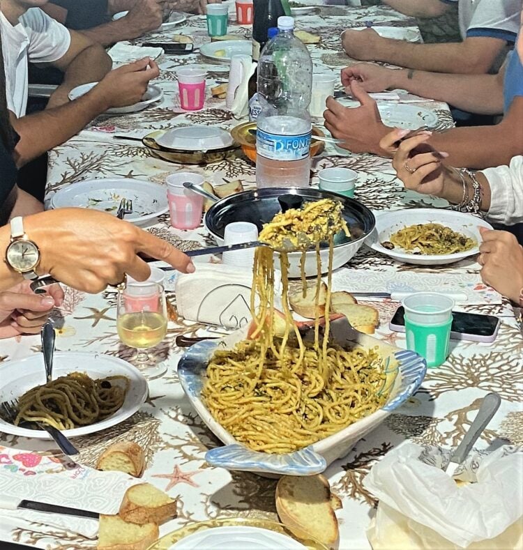 Table filled with plates, utensils and spaghetti being served.