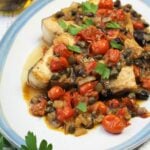 Plated swordfish steaks topped with cherry tomatoes, capers and olives.