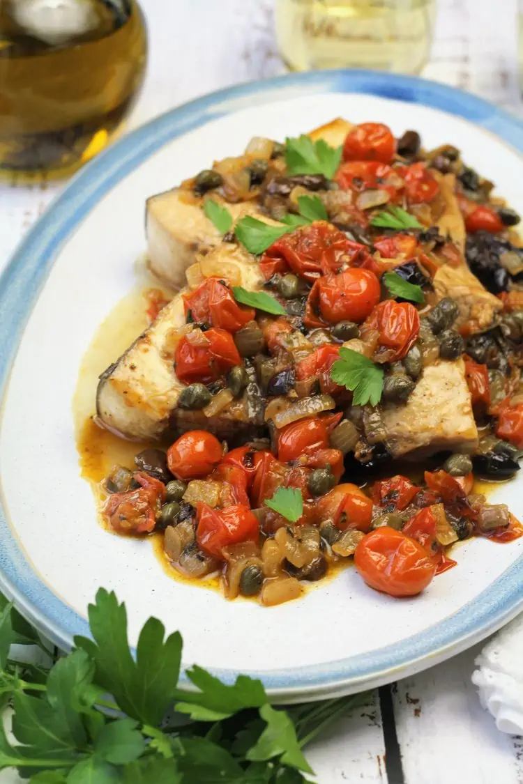 Plated swordfish steaks topped with cherry tomatoes, capers and olives.