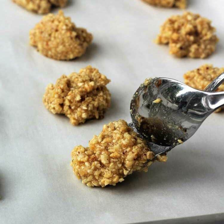 Dropping hazelnut cookie mixture onto baking sheet with spoons.
