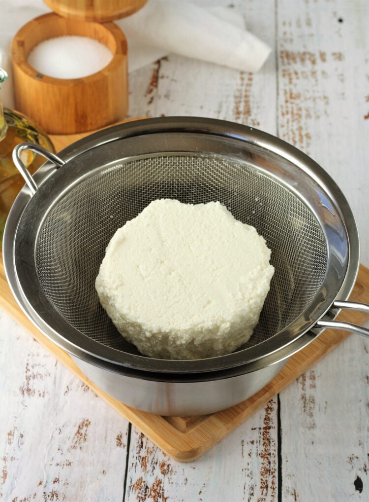 Whole ricotta in fine meshed sieve over bowl.