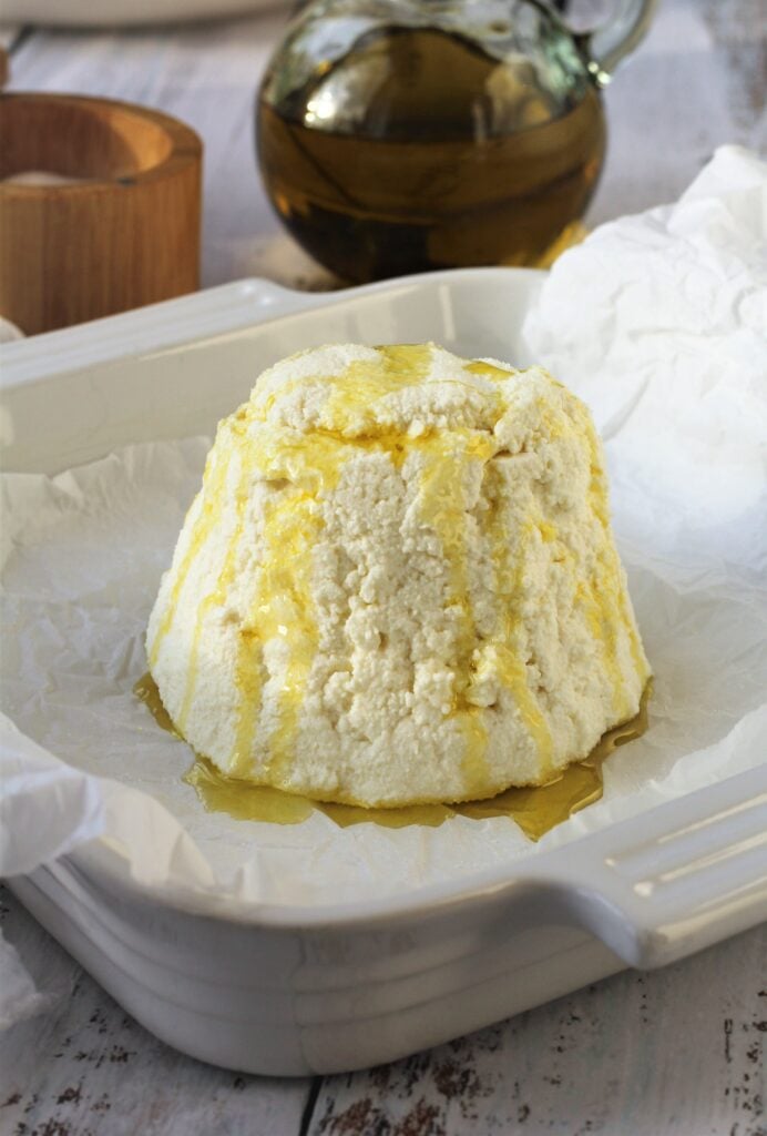 Whole ricotta with oil drizzled over it in baking dish.