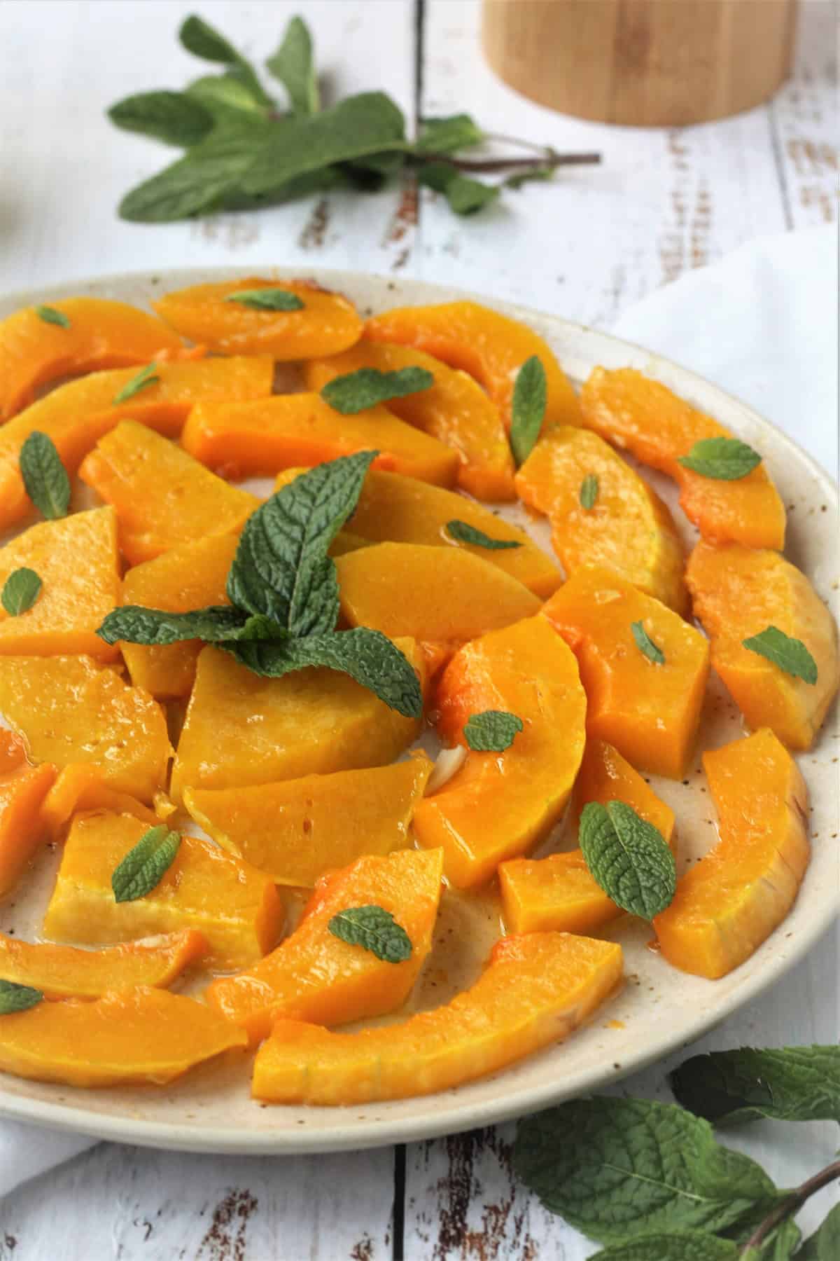 Sweet and sour squash slices topped with mint leaves on plate.