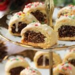 Fig filled Italian cookies with icing and nonpareils on tiered plate.