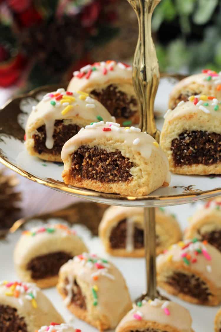 Fig filled Italian cookies with icing and nonpareils on tiered plate.