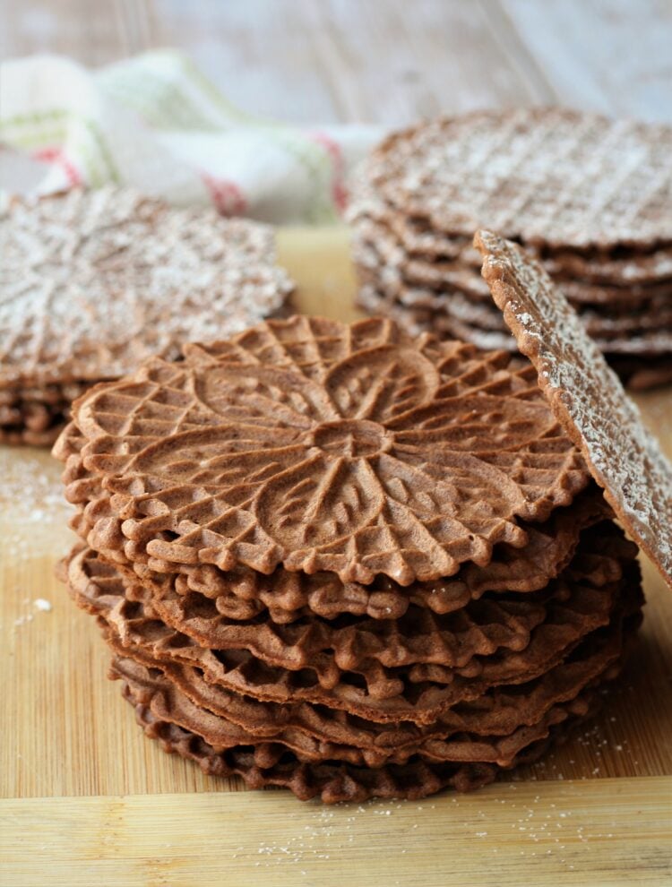 Piled chocolate pizzelle cookies on wood board.