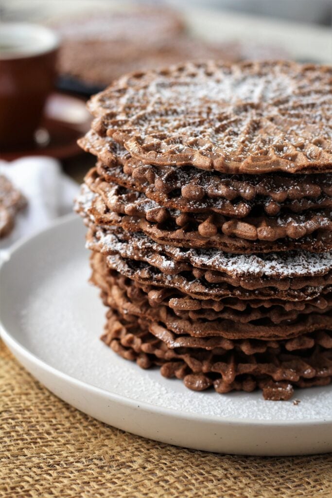 Stacked chocolate pizzelle cookies on round plate.