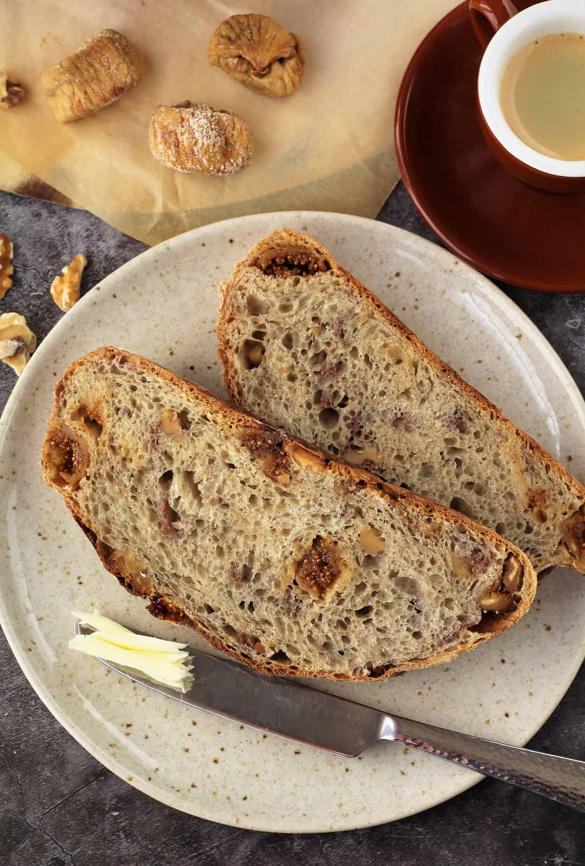 Slices of fig and walnut bread on plate with butter knife.